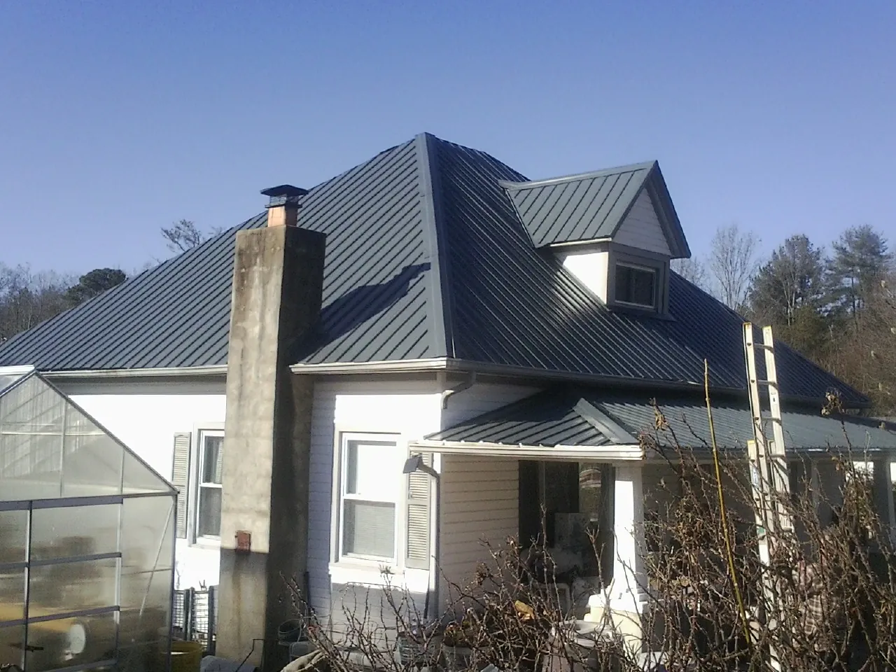 Dark blue standing seam metal roof on a white farmhouse with dormer — Slate & Tile Roof Repair by Roofing Brothers in Ayer