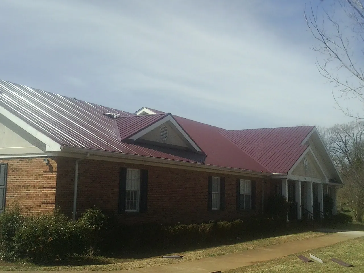 Red metal roof with gabled entries on a long brick building, from a Hail Damage Roof Repair job in Ayer
