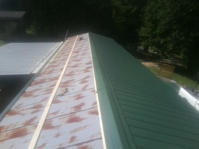 Old rusted panels beside newly installed green metal roofing — Wind Damage Roof Repair by Roofing Brothers in Ayer
