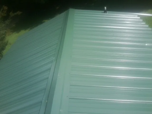 New green metal panels meeting at the ridge of a roof — Flat Roof Repair work by our crew in Ayer