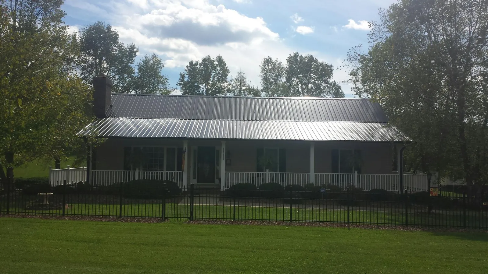 Gray metal roof on a brick ranch with a full width front porch — Gutter Guard Installation work by our crew in Ayer