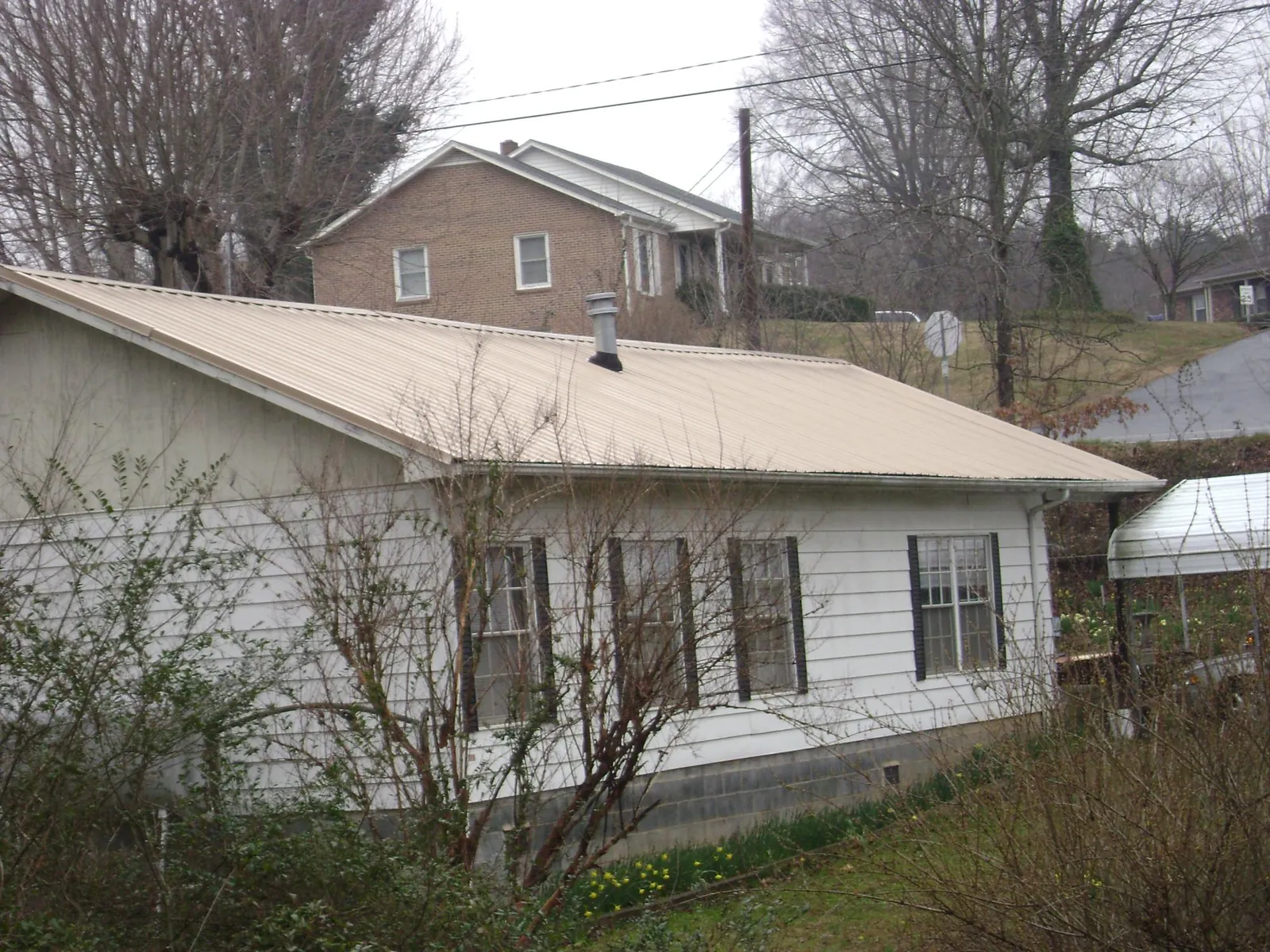 Tan metal roof on a white sided house set into a hillside — Commercial Roofing by Roofing Brothers in Ayer